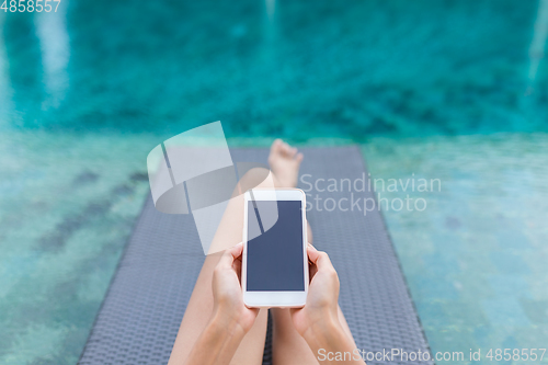 Image of Woman working on mobile phone at poolside on holiday