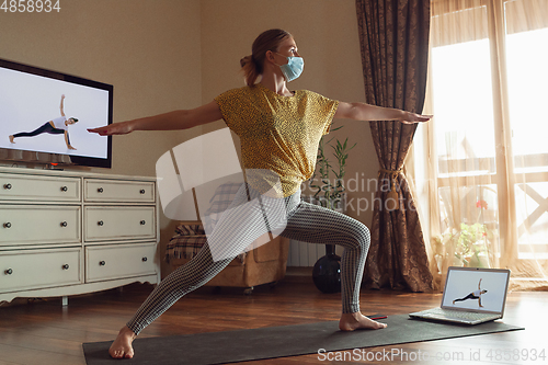 Image of Sporty young woman taking yoga lessons online and practice at home while being quarantine