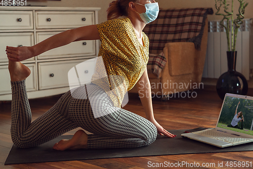 Image of Sporty young woman taking yoga lessons online and practice at home while being quarantine