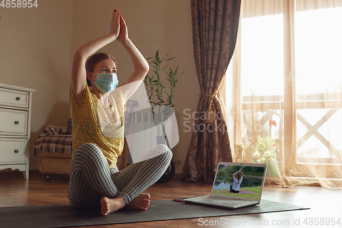 Image of Sporty young woman taking yoga lessons online and practice at home while being quarantine