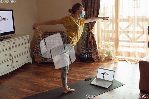 Image of Sporty young woman taking yoga lessons online and practice at home while being quarantine