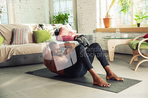 Image of Young african-american man teaching at home online courses of fitness, aerobic, sporty lifestyle while being quarantine