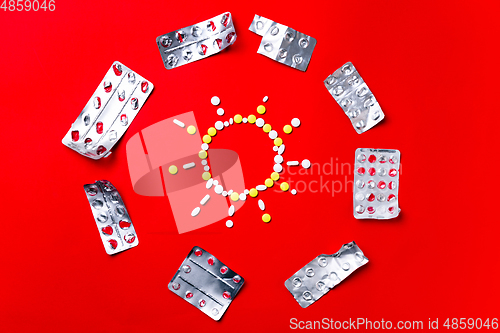 Image of Colored pills, tablets and capsules on a red background - history of treatment, prevention of pandemic