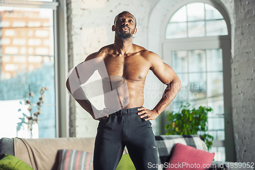 Image of Young african-american man teaching at home online courses of fitness, aerobic, sporty lifestyle while being quarantine