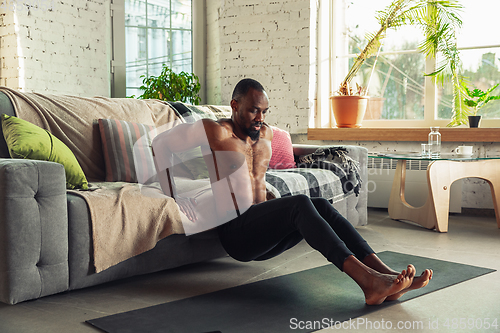 Image of Young african-american man teaching at home online courses of fitness, aerobic, sporty lifestyle while being quarantine