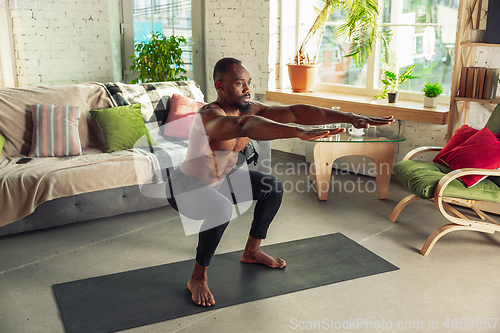 Image of Young african-american man teaching at home online courses of fitness, aerobic, sporty lifestyle while being quarantine