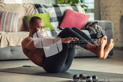 Image of Young african-american man teaching at home online courses of fitness, aerobic, sporty lifestyle while being quarantine