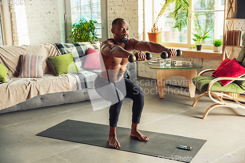 Image of Young african-american man teaching at home online courses of fitness, aerobic, sporty lifestyle while being quarantine