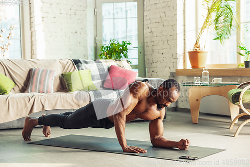 Image of Young african-american man teaching at home online courses of fitness, aerobic, sporty lifestyle while being quarantine