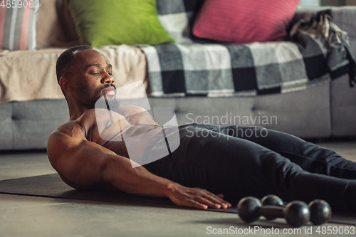 Image of Young african-american man teaching at home online courses of fitness, aerobic, sporty lifestyle while being quarantine