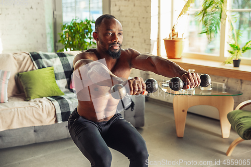 Image of Young african-american man teaching at home online courses of fitness, aerobic, sporty lifestyle while being quarantine