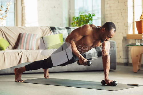 Image of Young african-american man teaching at home online courses of fitness, aerobic, sporty lifestyle while being quarantine