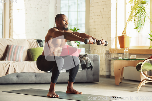 Image of Young african-american man teaching at home online courses of fitness, aerobic, sporty lifestyle while being quarantine