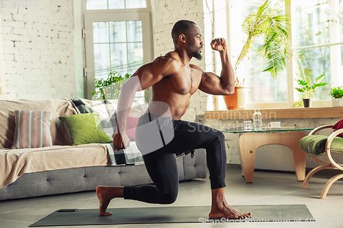 Image of Young african-american man teaching at home online courses of fitness, aerobic, sporty lifestyle while being quarantine