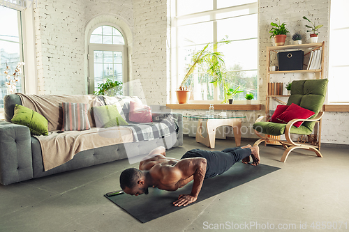 Image of Young african-american man teaching at home online courses of fitness, aerobic, sporty lifestyle while being quarantine