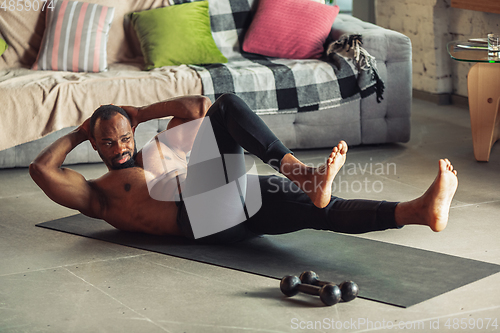 Image of Young african-american man teaching at home online courses of fitness, aerobic, sporty lifestyle while being quarantine