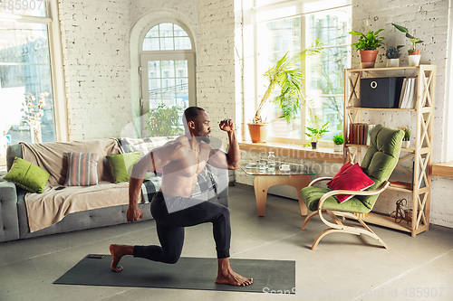 Image of Young african-american man teaching at home online courses of fitness, aerobic, sporty lifestyle while being quarantine