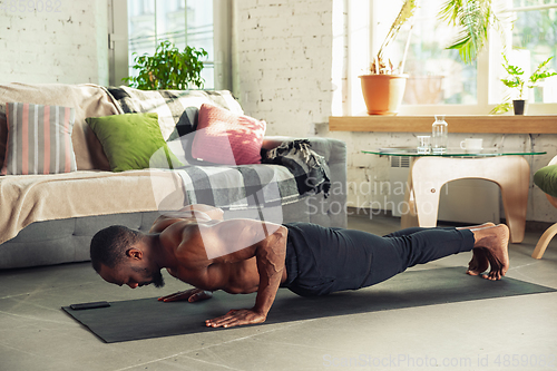 Image of Young african-american man teaching at home online courses of fitness, aerobic, sporty lifestyle while being quarantine