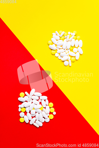 Image of Colored pills, tablets and capsules on a red and yellow background - history of treatment, prevention of pandemic