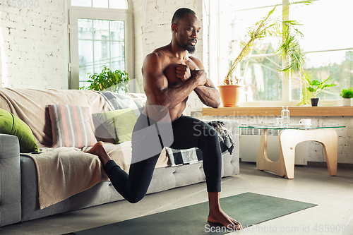 Image of Young african-american man teaching at home online courses of fitness, aerobic, sporty lifestyle while being quarantine