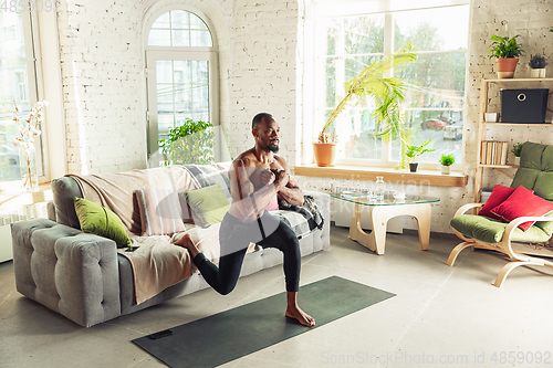 Image of Young african-american man teaching at home online courses of fitness, aerobic, sporty lifestyle while being quarantine