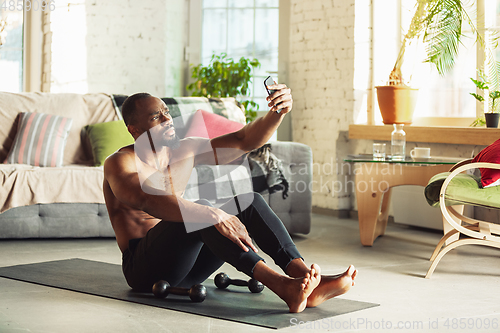 Image of Young african-american man teaching at home online courses of fitness, aerobic, sporty lifestyle while being quarantine