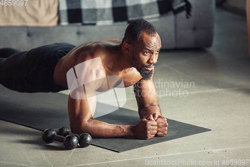 Image of Young african-american man teaching at home online courses of fitness, aerobic, sporty lifestyle while being quarantine