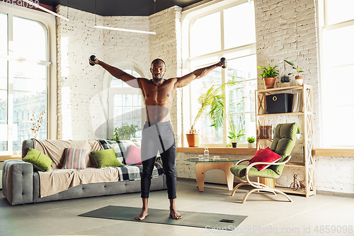 Image of Young african-american man teaching at home online courses of fitness, aerobic, sporty lifestyle while being quarantine