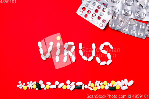 Image of Colored pills, tablets and capsules on a red background - history of treatment, prevention of pandemic