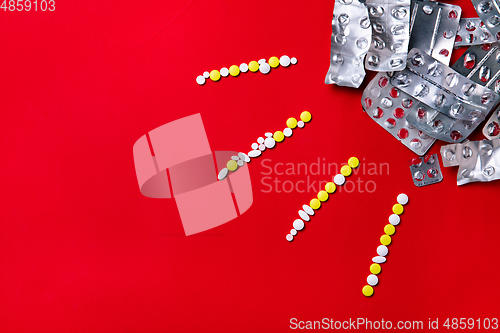 Image of Colored pills, tablets and capsules on a red background - history of treatment, prevention of pandemic