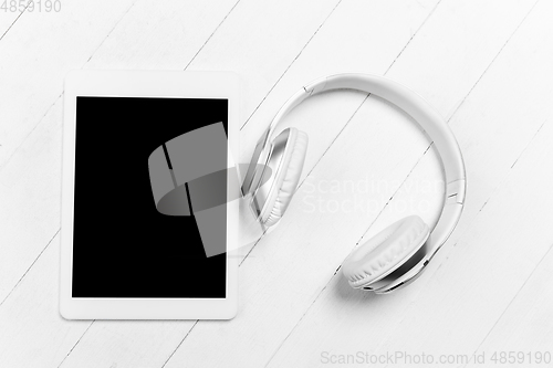 Image of Tablet and headphones. Monochrome stylish composition in white color. Top view, flat lay.