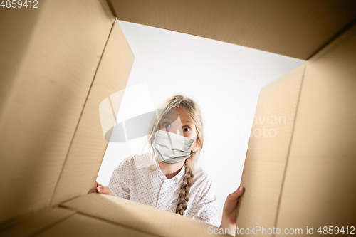 Image of Little girl opening the huge postal package wearing protective face mask, contactless delivery