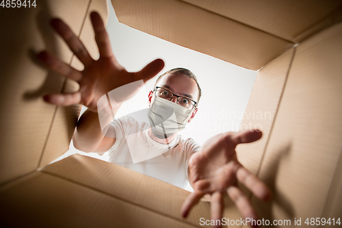 Image of Young man opening the huge postal package wearing protective face mask, contactless delivery