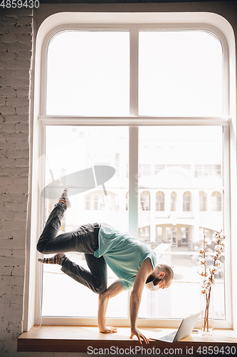 Image of Young man doing yoga at home while being quarantine and freelance working