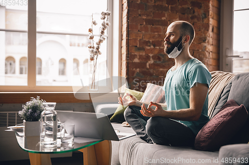 Image of Young man doing yoga at home while being quarantine and freelance working