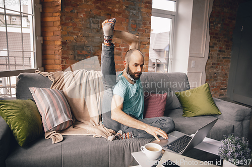 Image of Young man doing yoga at home while being quarantine and freelance working