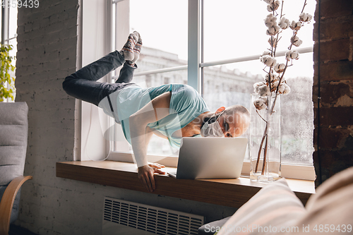 Image of Young man doing yoga at home while being quarantine and freelance working