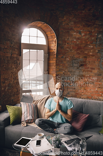 Image of Young man doing yoga at home while being quarantine and freelance working