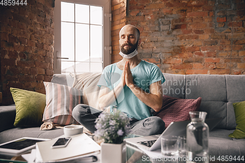 Image of Young man doing yoga at home while being quarantine and freelance working