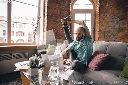 Image of Young man doing yoga at home while being quarantine and freelance working