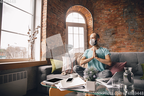 Image of Young man doing yoga at home while being quarantine and freelance working