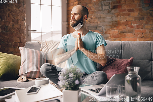 Image of Young man doing yoga at home while being quarantine and freelance working