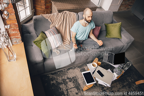 Image of Young man doing yoga at home while being quarantine and freelance working