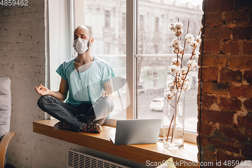 Image of Young man doing yoga at home while being quarantine and freelance working