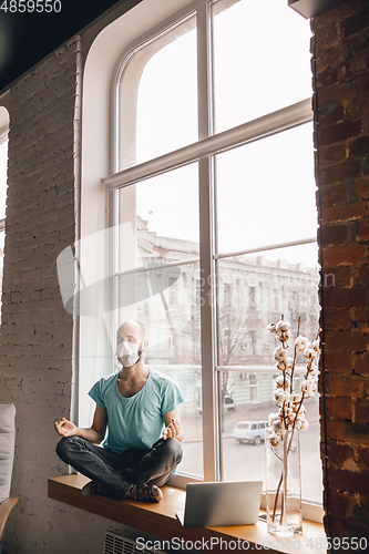 Image of Young man doing yoga at home while being quarantine and freelance working