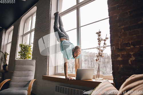 Image of Young man doing yoga at home while being quarantine and freelance working