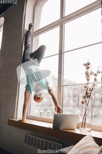 Image of Young man doing yoga at home while being quarantine and freelance working