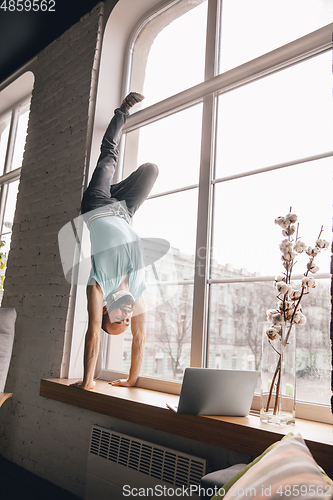 Image of Young man doing yoga at home while being quarantine and freelance working