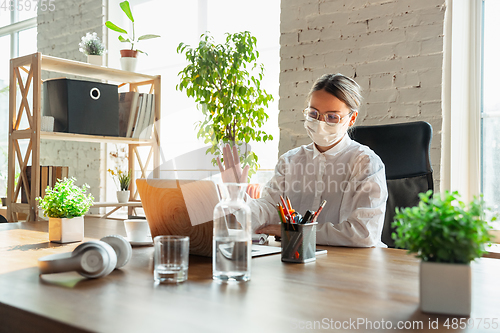 Image of Woman working in office alone during coronavirus or COVID-19 quarantine, wearing face mask