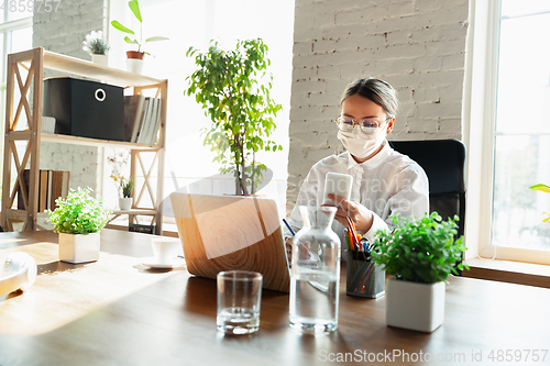 Image of Woman working in office alone during coronavirus or COVID-19 quarantine, wearing face mask